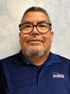 Pest control technician wearing glasses and a navy Thrasher polo against a neutral backdrop