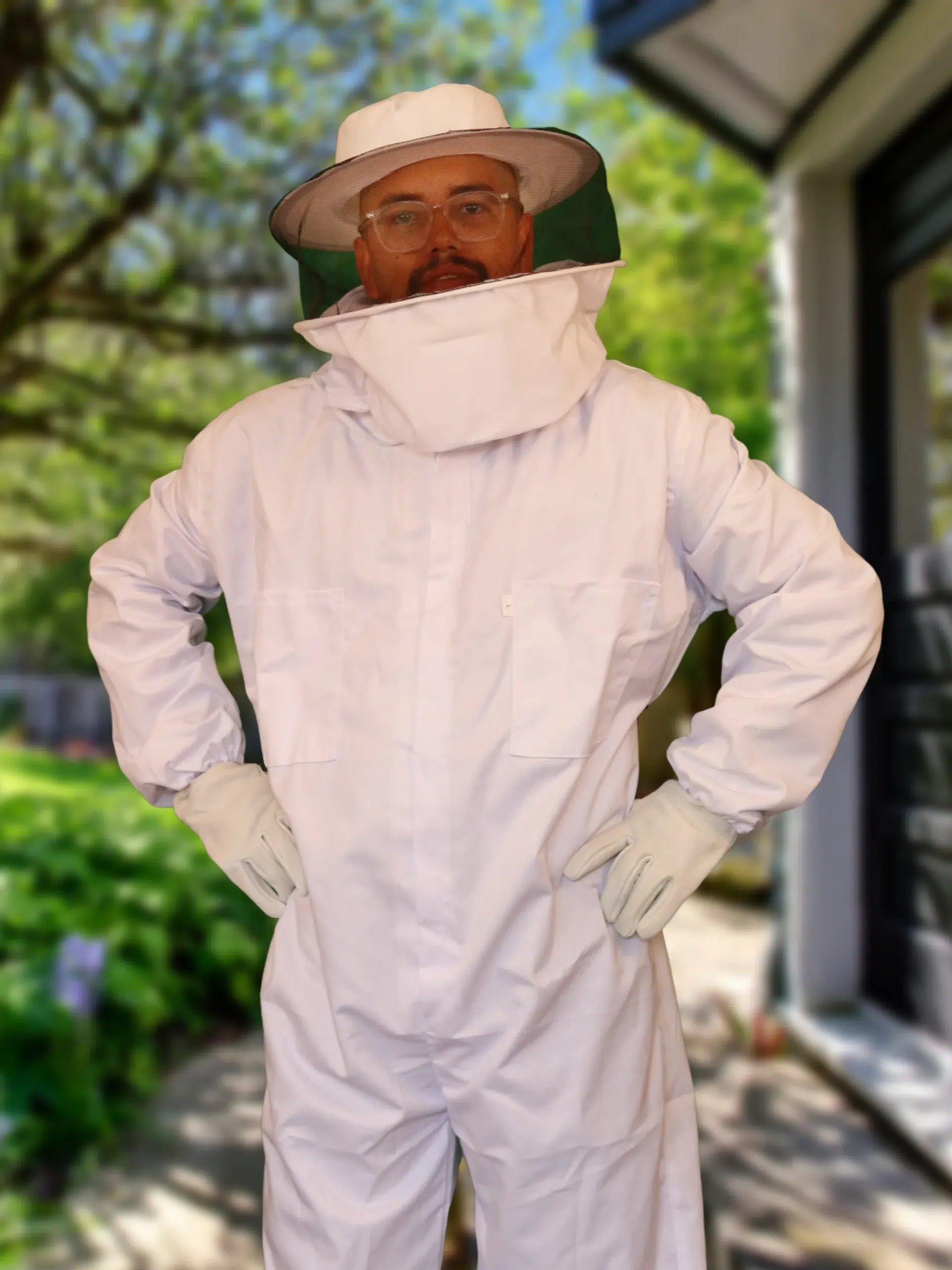 Pest control technician wearing a white protective suit, hat with veil and gloves standing outdoors