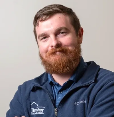 Man with red beard wearing Thrasher Pest Control jacket, arms crossed and slight smile