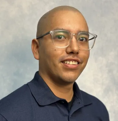 Man wearing navy Thrasher Pest Control polo, clear-frame glasses, smiling at camera