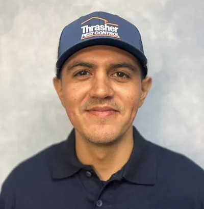 Close-up portrait of a man wearing a Thrasher Pest Control cap and polo shirt, slight smile