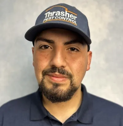 Person wearing Thrasher Pest Control cap and polo with company logo, close-up from chest to forehead
