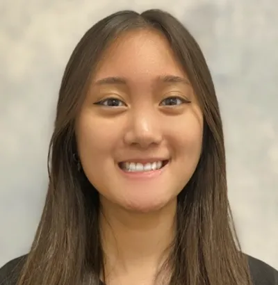 Smiling young woman with long straight hair wearing a black top against a soft gray backdrop