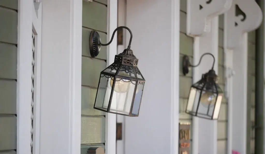 Two wall-mounted glass porch lanterns on a home's exterior, one in sharp focus and one blurred behind it