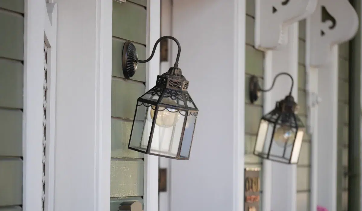 Two wall-mounted glass porch lanterns on a home's exterior, one in sharp focus and one blurred behind it
